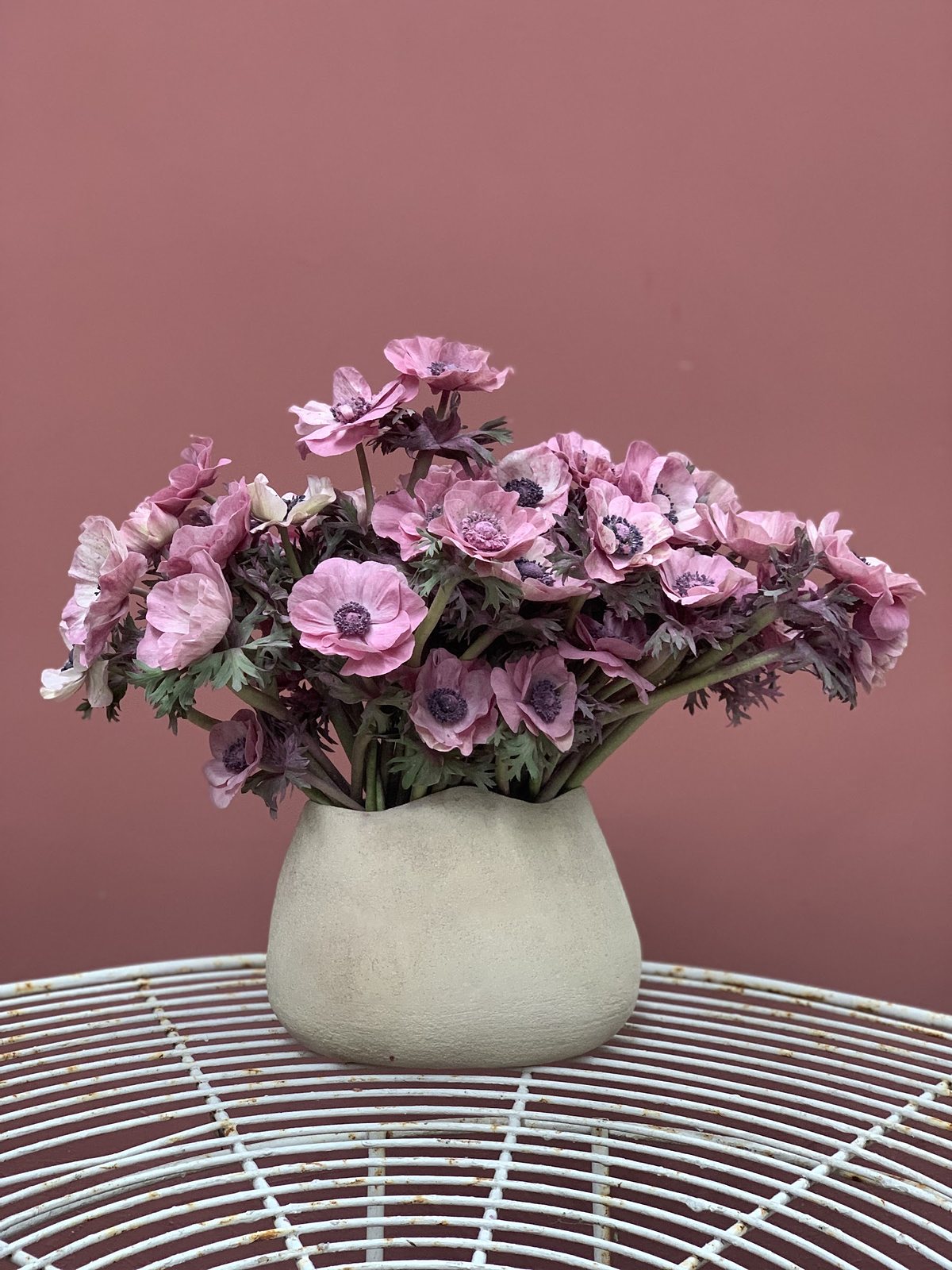 Bouquet rose et blanc dans un vase clair, posé sur un guéridon devant un mur rose