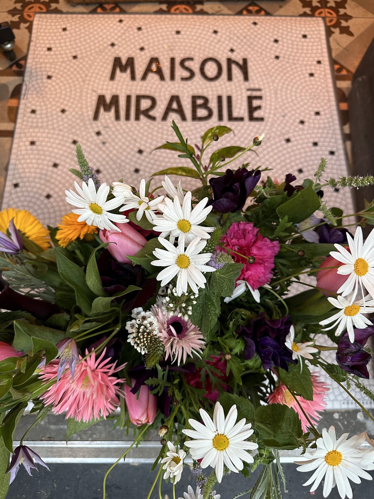 L’enseigne en tissu rose à pois de la maison, au-dessus d’un bouquet de marguerites et de gerberas