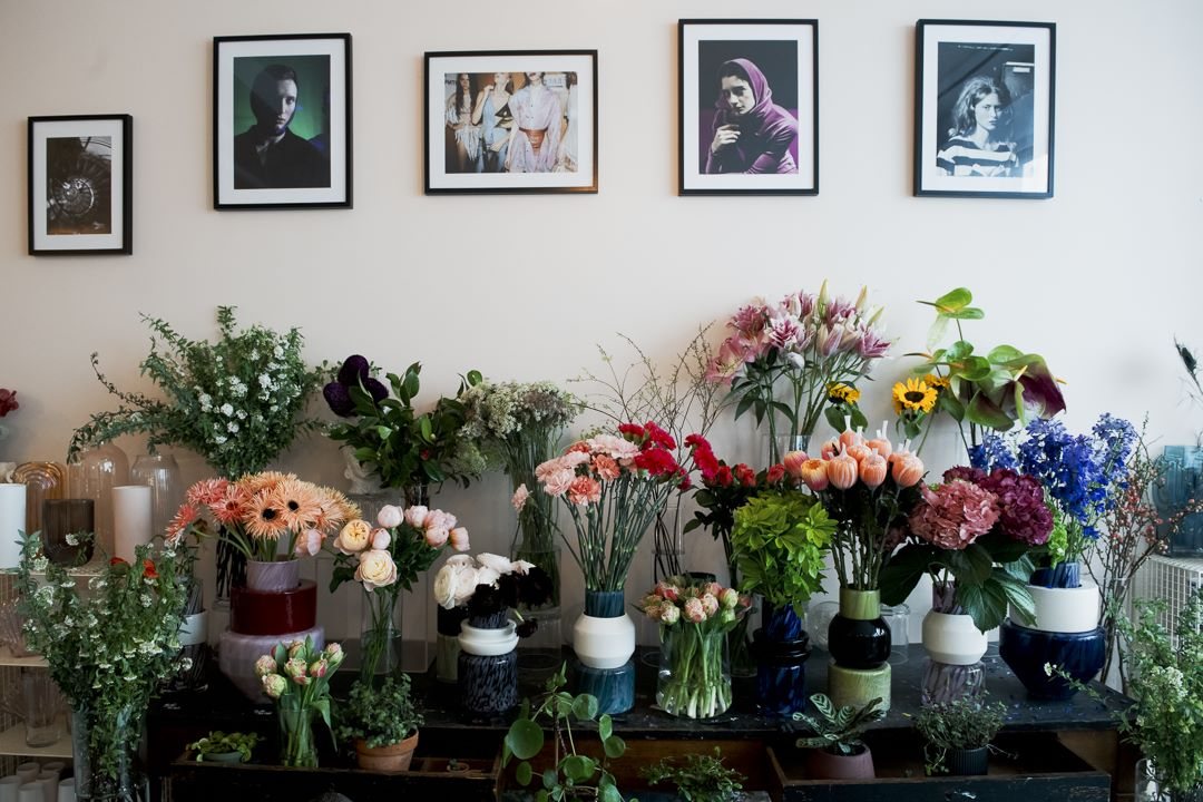 Un mur de photographies encadrées au-dessus des seaux de fleurs coupées