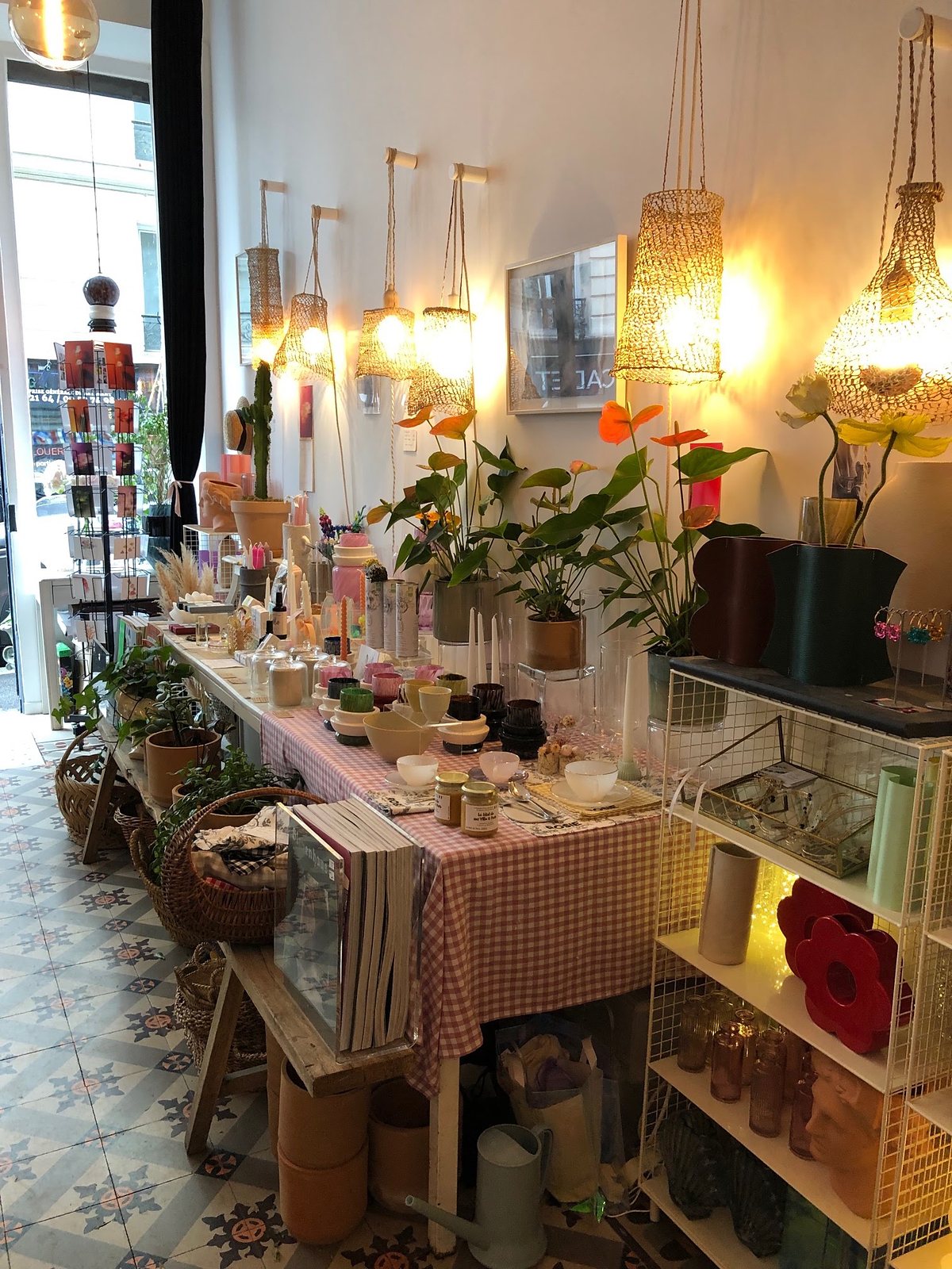 L’intérieur de la boutique : tables garnies d’objets, suspensions perlées allumées et carreaux de ciment