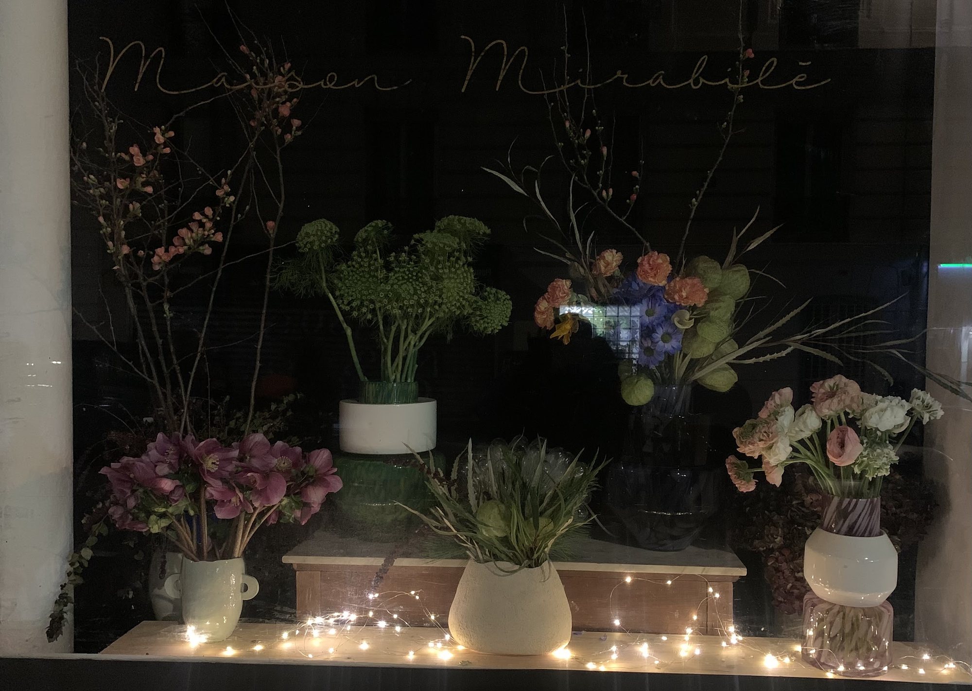 La vitrine le soir, le nom de la maison écrit à la main sur la vitre au-dessus des branches en fleur