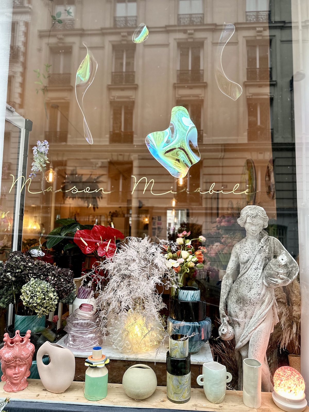 Vitrine de la galerie : vases, céramiques et sculptures de verre irisé suspendues devant la rue